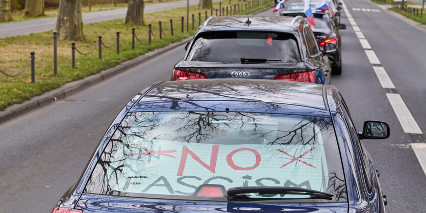 Durch die Rückscheibe eines PKW liest man das Plakat "No Fascism" mit durchgestrichenem Nato-Symbol