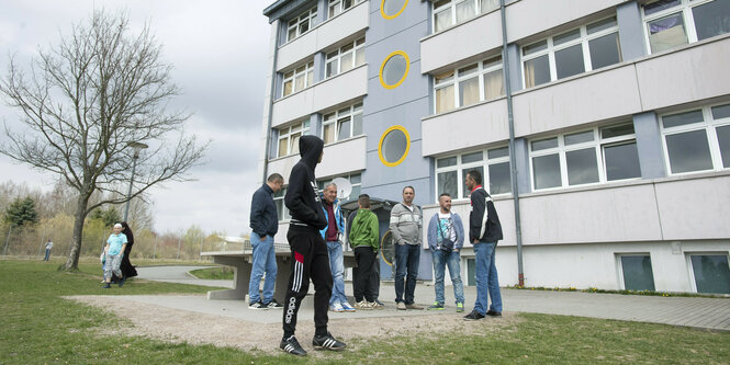 Männer stehen vor einem Gebäude, alle haben die HÄnde in den Hosentaschen