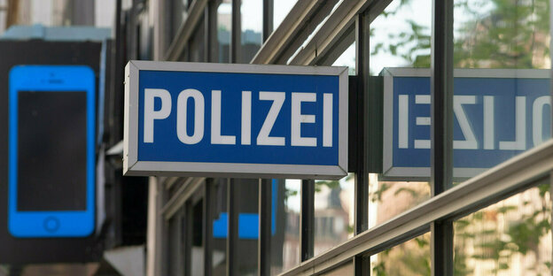 blaues Schild mit POLIZEI Aufschrift in weiß an einem Gebäude