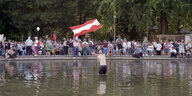 Mann mit nacktem Oberkörper schwingt Österreich-Fahne in einem Brunnen