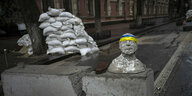 Eine Skulptur mit Stirnband in den Farben der ukrainischen Flagge, dahinter Sandsäcke