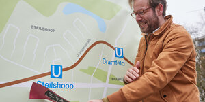 Anjes Tjarks steht vor einem Plakat, dass den Streckenverlauf der U5 zeigt