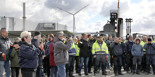 Menschengruppe vor Industrieanlage und Windrad.