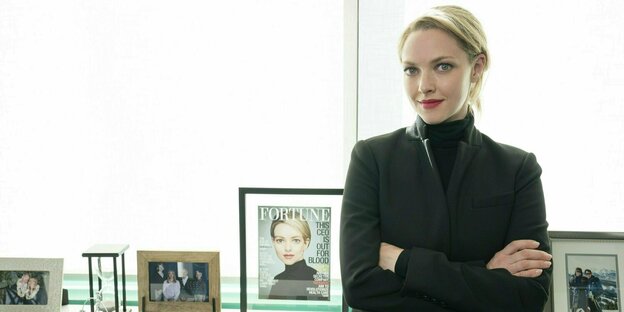 Eine blonde Frau in schwarzem Jacket steht vor einem Fenster. Auf der Fensterbank sind Bilderrahmen, in denen sich Fmailienfotos und ein Zeitungscover befinden, das die Frau in der Vogue zeigt.