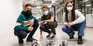 Drei SchülerInnen hocken vor ihren kleinen Robotern auf dem Boden