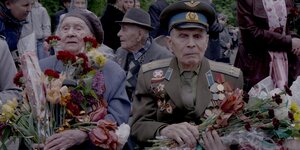 Ein alter Mann und eine Frau, dekoriert mit Orden, haben Blumensträuße in der Hand