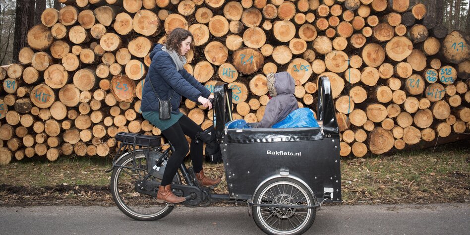 Eine Frau mit Lastenrad und Kind vor einem Holzstapel