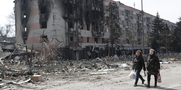 Zwei Frauen gehen in der Nähe von beschädigten Gebäuden in Mariupol entlang Zwei Frauen gehen in der Nähe von beschädigten Gebäuden in Mariupol entlang