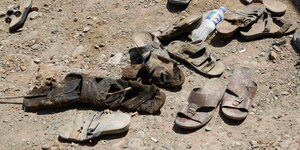 Mehrere abgetragene, schmutzige Schuhe liegen auf Sand.