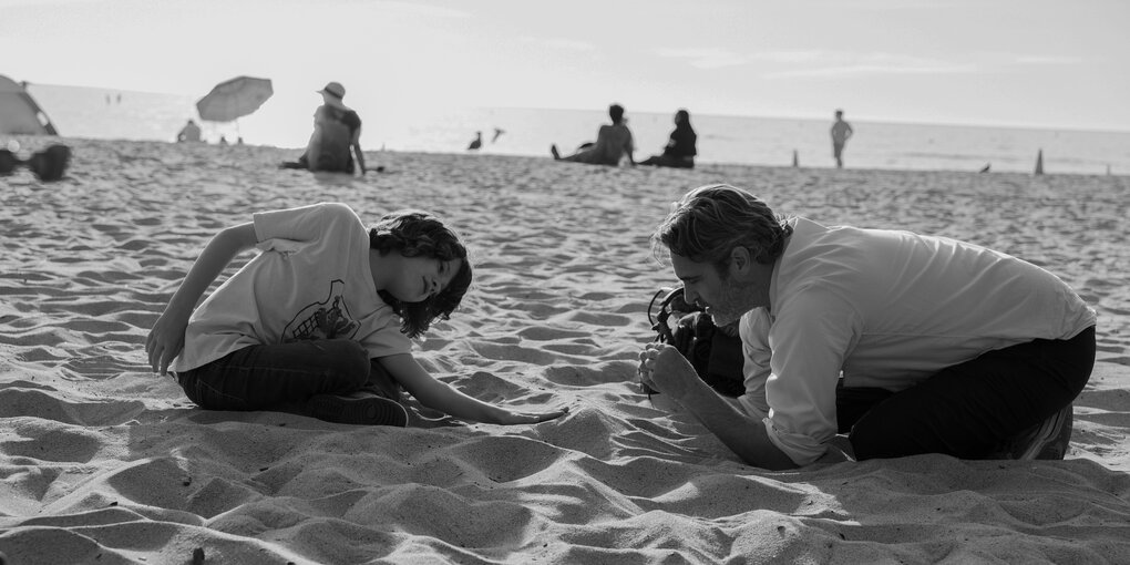 Ein Kind und ein Erwachsener knien im Sand und graben darin