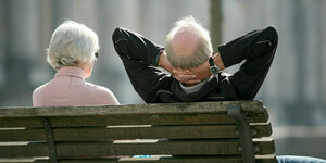 Eine älterer Herr und eine ältere Dame sitzen auf einer Parkbank in der Sonne