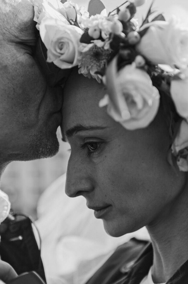 Eine Frau wird von einem Mann geküsst auf die Stirn, ihr Haar ist mit einem Blumenkranz geschmückt
