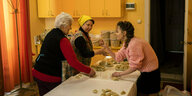 Drei Frauen bereiten in einer Küche Teigtaschen zu