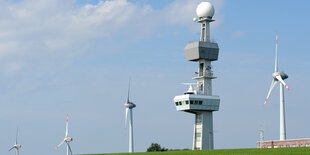 Windräder stehen neben einer Radaranlage hinter einem Deich