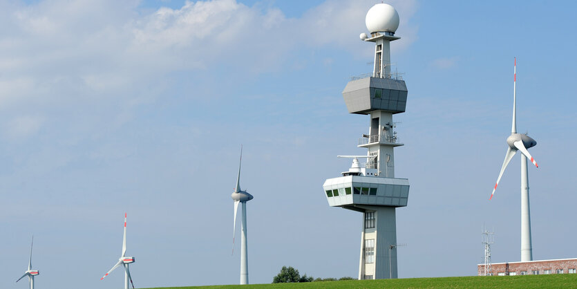 Windräder stehen neben einer Radaranlage hinter einem Deich