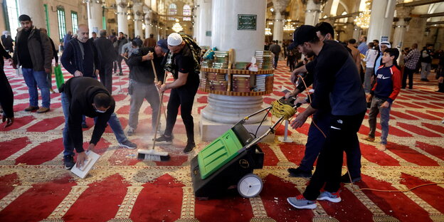 Drei Männer – einer mit Besen und einer mit Kehrmaschine – säubern den Boden der Al-Aqsa-Moschee von Steinen und anderen Hinterlassenschaften der vorherigen Auseinandersetzung.