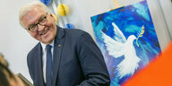 Bundespräsident Steinmeier lachend vor einem Gemälde der Friedenstaube