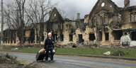 Eine Frau geht mit Gepäck an einer völlig zerstörten Hauserfront vorbei