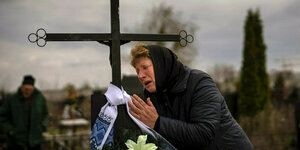 Eine Frau in Trauer an einem Grab mit Kreuz