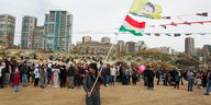 Ein Mann schwingt vor feiernden Menschen Fahnen mit der Flagge Kurdistans und einem Bild ihres Anführers