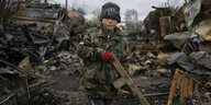 7-jähriger Junge steht vor einem zerstörten Panzer mit einem Holzgewehr in der Hand