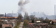 Zertrümmerte Häuser, im Hintergrund ein Brand und ein Stahlwerk