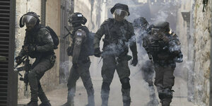 Vier so gut wie vermummte israelische Soldaten stehen in einer von historisch aussehenden Gebäuden gesäumten Straße