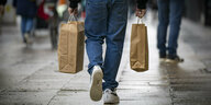 Ein Mann geht über eine Straße in der City-West und trägt in den Händen zwei Einkaufstaschen