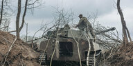 Ein Panzer im Wald, ukrainischer Soldat bedeckt ihn mit Ästen