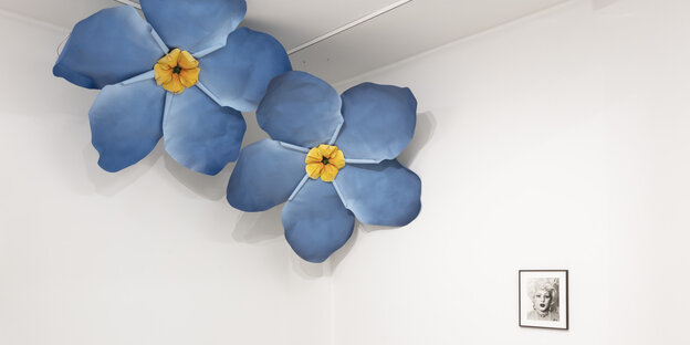 Zwei riesiege blaue Blüten aus Stoff hängen unter der Decke, darunter eine Schwarzweißfotografie