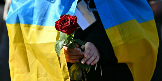 Eine Frau mit ukrainischer Flagge hält eine Rose in der Hand