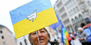 Eine Frau hält ein Schild mit ukrainischer Flagge und Friedenstaube hoch