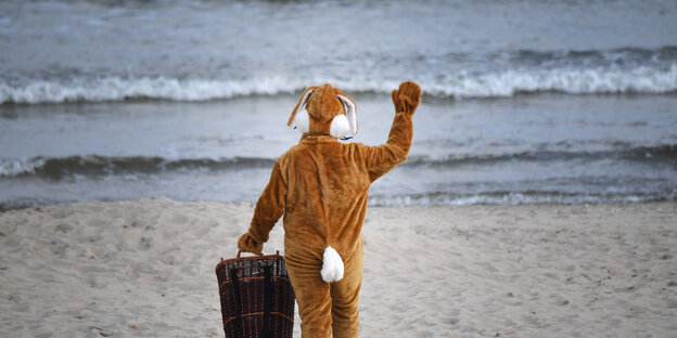 Ein Mann winkt in einem Osterhasen-Kostüm am Strand von Zinnowitz auf der Insel Usedom.