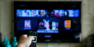 Ein Mann hält eine Fernbedienung in der Hand und zeigt auf einen TV-Bildschirm