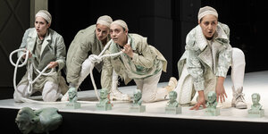 Vier Frauen in grauen Kostümen hantieren am Bühnenrand geduckt mit einem Seil