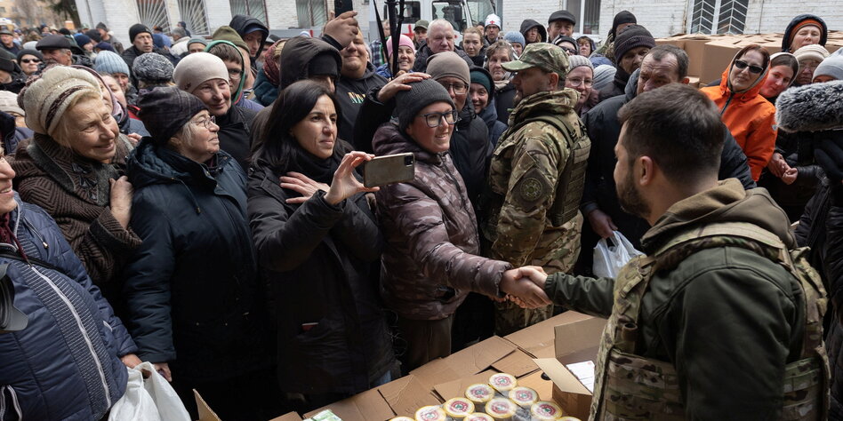 Ein Mann in Armeekleidung spricht zu einer Menschengruppe, Präsident Selenski in Butscha