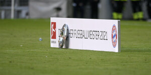 Ein Schild auf dem Rasen, darauf steht: "Deutscher Fußballmeister 2021", daran gelehnt: die Meisterschale