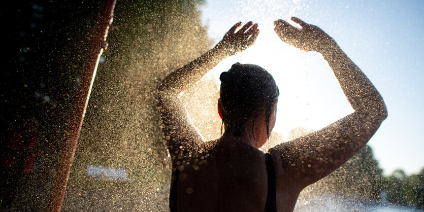 Person unter Freibaddusche im Gegenlicht