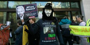 Ein Demonstrant mit Anonymous-Maske und einem Schild das Julian Assange mit Maulkorb zeigt