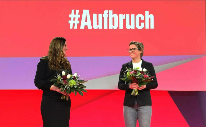 Janine Wissler und Susanne Henning-Wellsow mit Blumen vor dem Parteitagslogo #Aufbruch