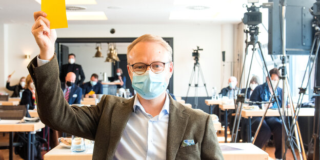 Michael Kruse mit Mund-Nasen-Schutz hält während eines Online-Parteitags der Hamburger FDP seine Stimmkarte hoch