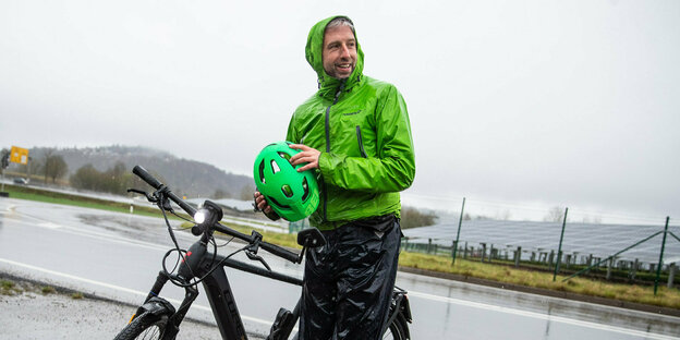 Boris Palmer steht mit seinem Fahrrad und einer grünen Jacke im Regen.