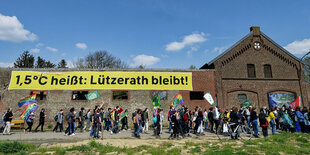 Viele Menschen ziehen an einer Hausfassade vorbei, an der hängt ein Transpi mit der Aufschrift "1,5 Grad heißt - Lützerath bleibt"