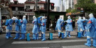 Männer in blauen Schutzanzügen hantieren auf einer Straße mit Kanistern