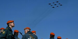 Soldaten mit roten Mützen schauen auf Kampfjets am Himmel