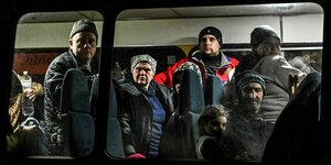 Männer, Frauen und ein Kind sehten und sitzen in einem vollen Bus und schauen erschöpft aus dem Fenster
