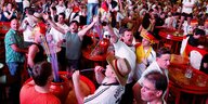 Das Innere vom Bierkönig. Ungezählte Menschen stehen neben und auf Tischen. Sie trinken Alkohol, tanzen und grölen. Viele von ihnen tragen Deutschlandtrikots oder anderen Merchandise der deutschen Nationalmannschaft wie etwa riesige Hüte.