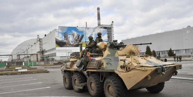 Soldaten sitzen auf einem Panzer, im Hintergrund das Atomkraftwerk Tschernobyl