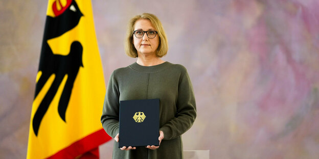 Lisa Paus hält ihre Ernennungsurkunde in der Hand, dahinter eine Deutschlandfahne