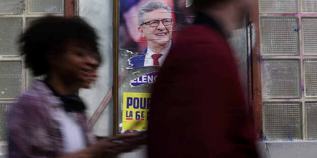 Junge Menschen gehen an einem Wahlplakat von Melenchon vorbei